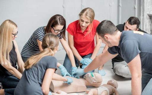Group of people learning how to make first aid heart compressions with dummies during the training indoors